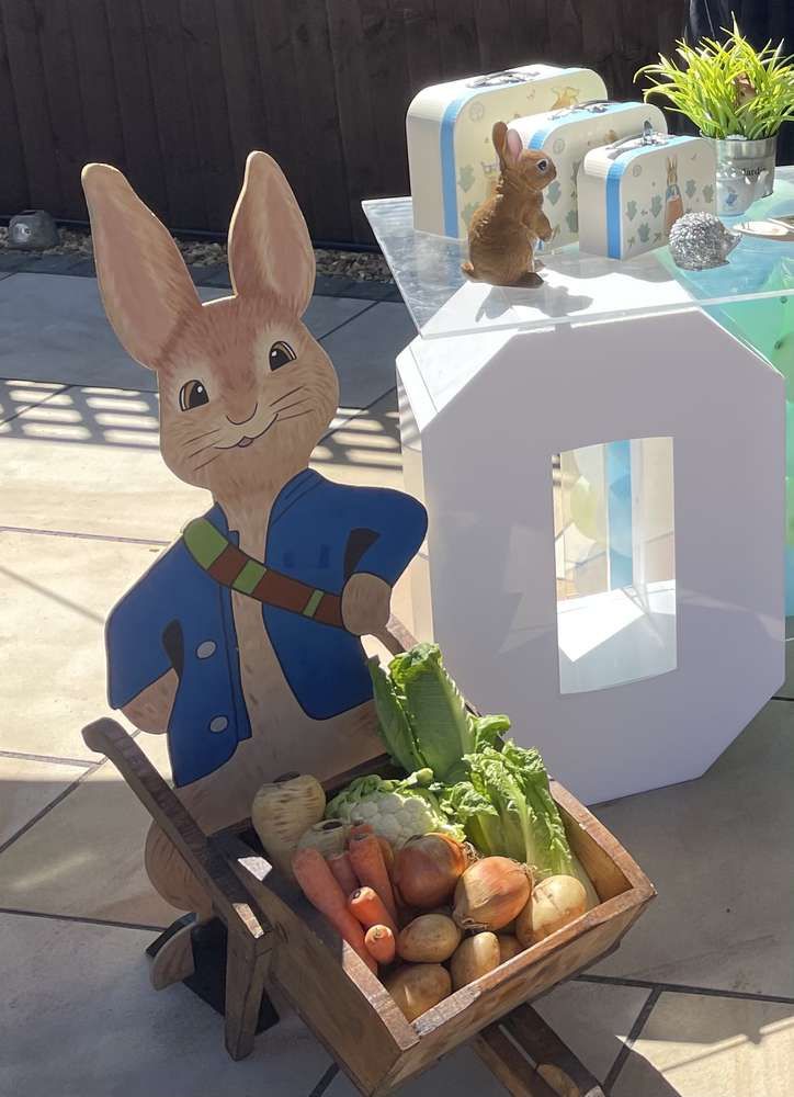 a wooden cart filled with vegetables next to a statue of a rabbit holding a carrot