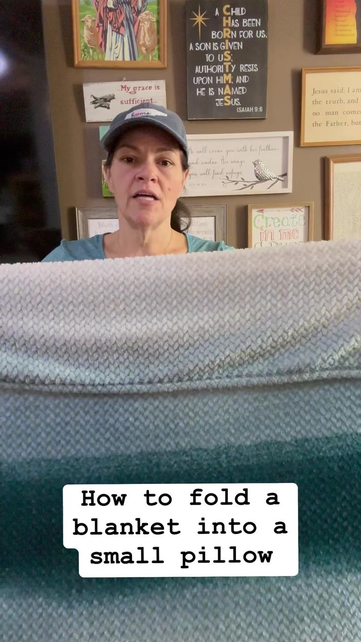 a woman holding up a blanket in front of a wall with pictures on it and the words how to fold a blanket into a small pillow