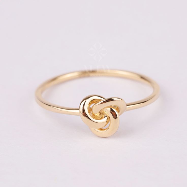 a gold ring with an intertwined knot on the front and center, sitting on a white surface