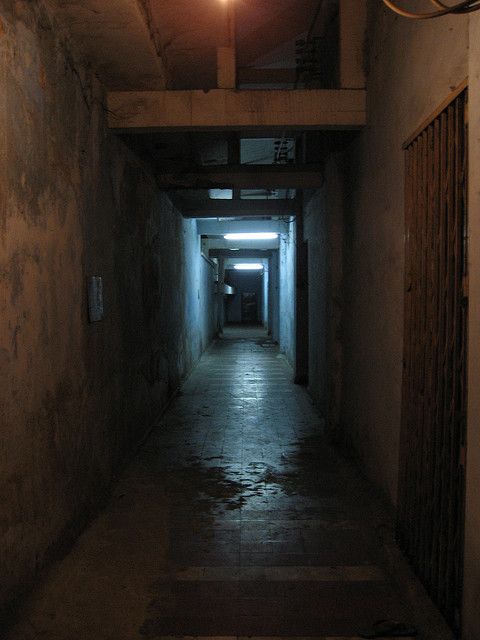 a dark hallway with light at the end and no one in sight on the other side