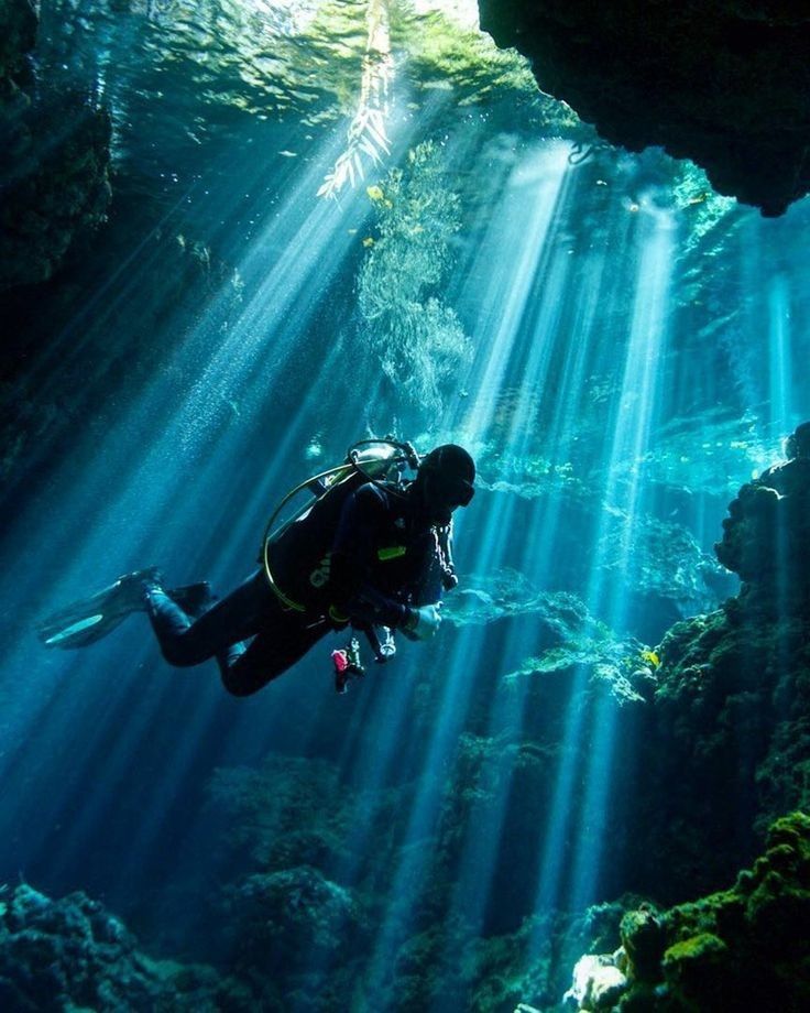 a scuba diver swims through the water in an underwater cave with sunbeams