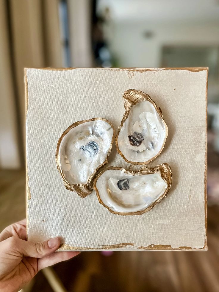 a person holding up a piece of art with three oysters on it's surface