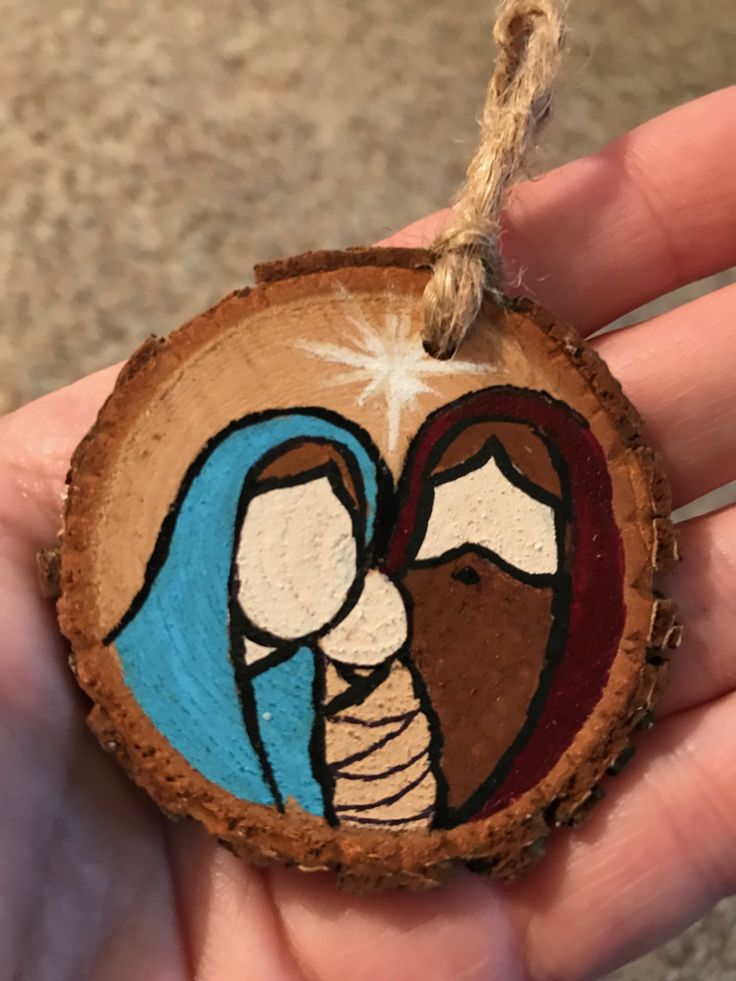 a hand holding a wooden ornament with a nativity scene painted on it