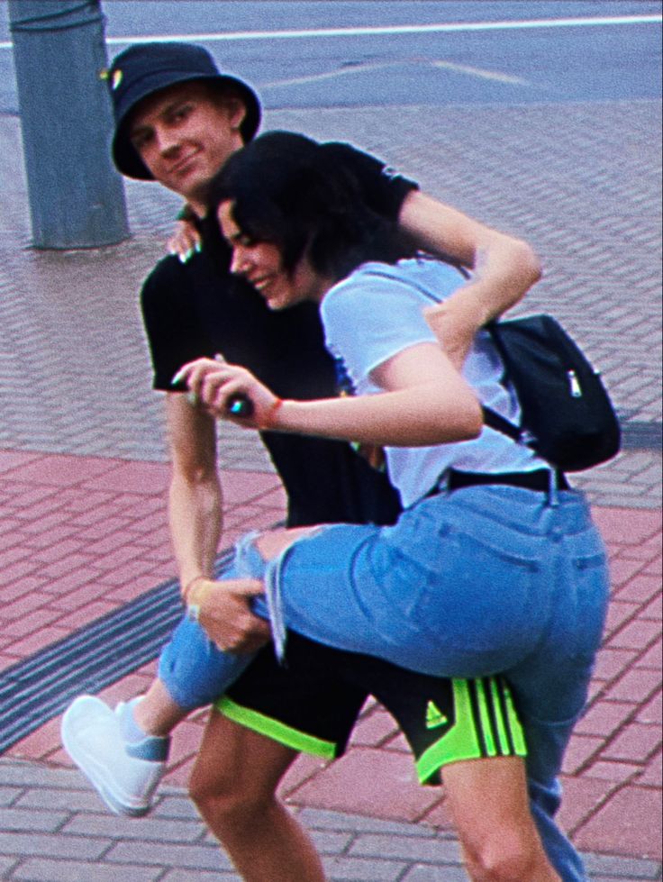 two young people are riding on a skateboard down the street while one person is holding onto another man's back