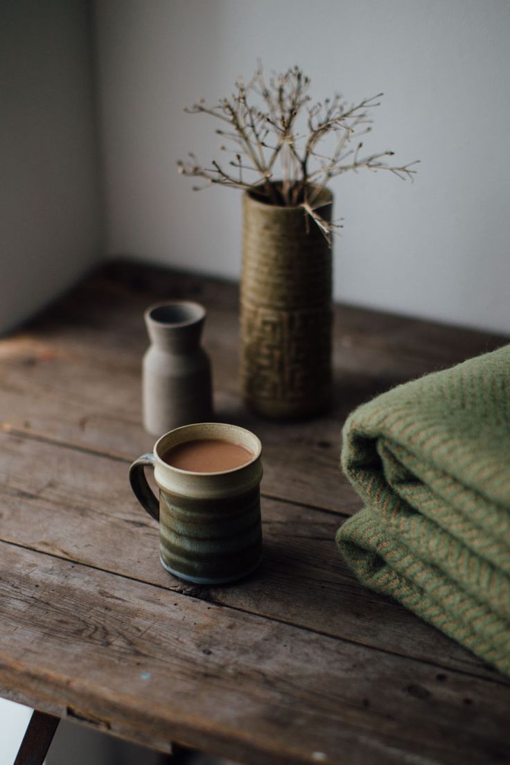 a cup of coffee sitting on top of a wooden table next to two vases