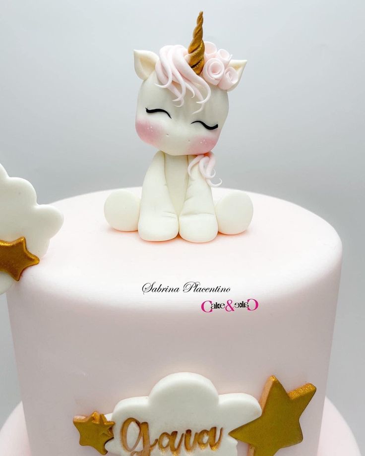 a white cake with pink frosting and gold stars on top that has a small unicorn sitting on top of it