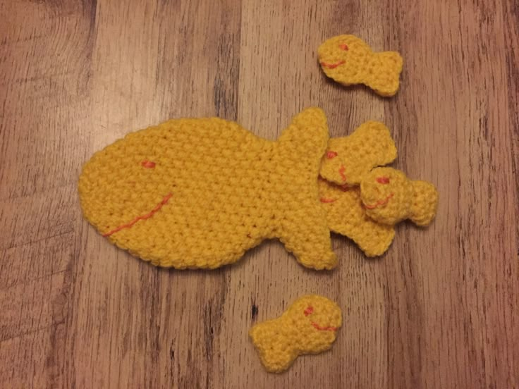 a crocheted yellow teddy bear laying on top of a wooden floor next to two smaller ones