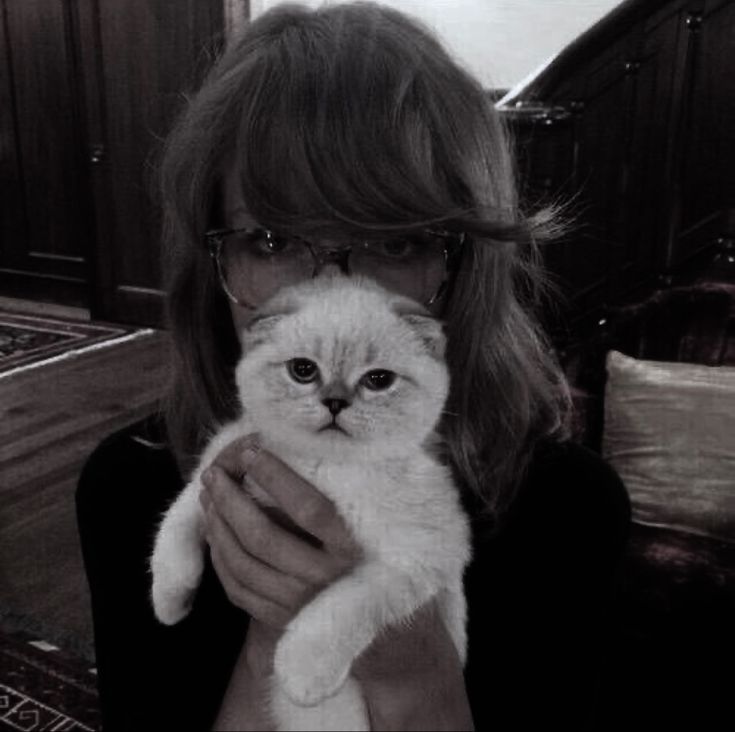 a black and white photo of a woman holding a cat in her hands with glasses on