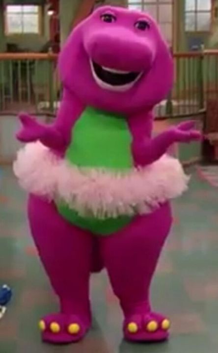 the purple dinosaur is wearing a green shirt and pink tutu while standing on one foot