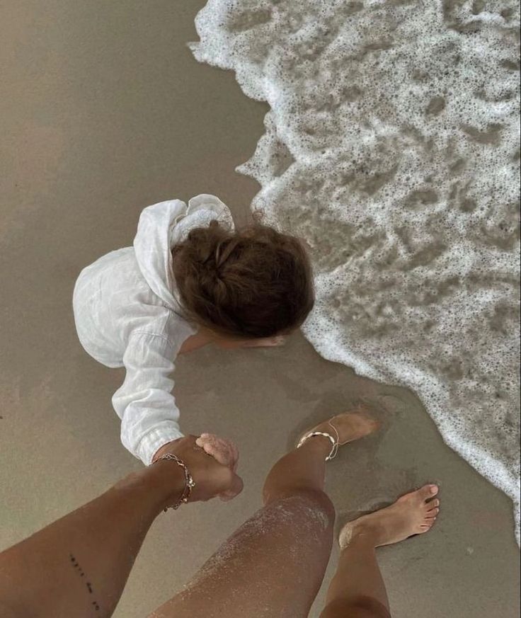 two people standing on the beach with their feet in the sand and one is wearing a white shirt