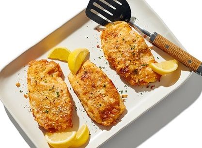 two fish fillets on a plate with lemons and a spatula next to them