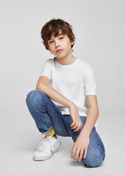 a young boy sitting on the ground wearing jeans and a white t - shirt