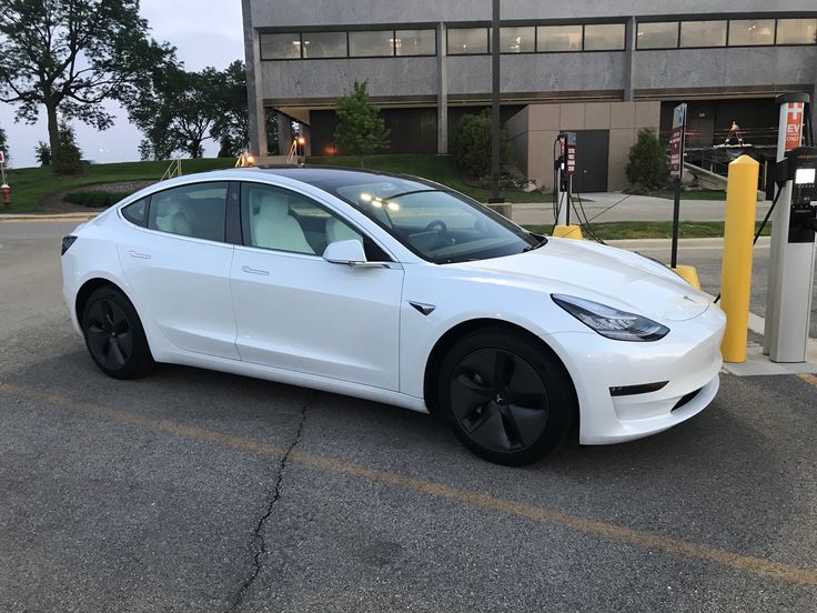 a white tesla electric car parked in front of a building with an open gas pump