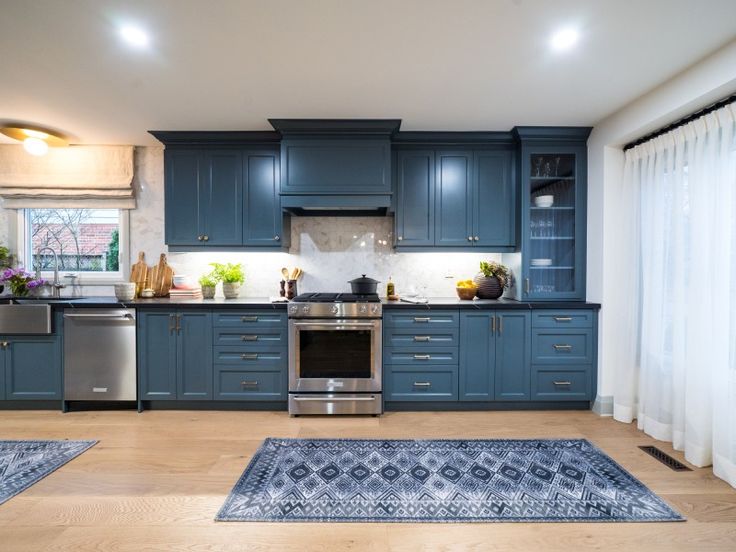 a kitchen with blue cabinets and stainless steel appliances, rugs in front of the stove