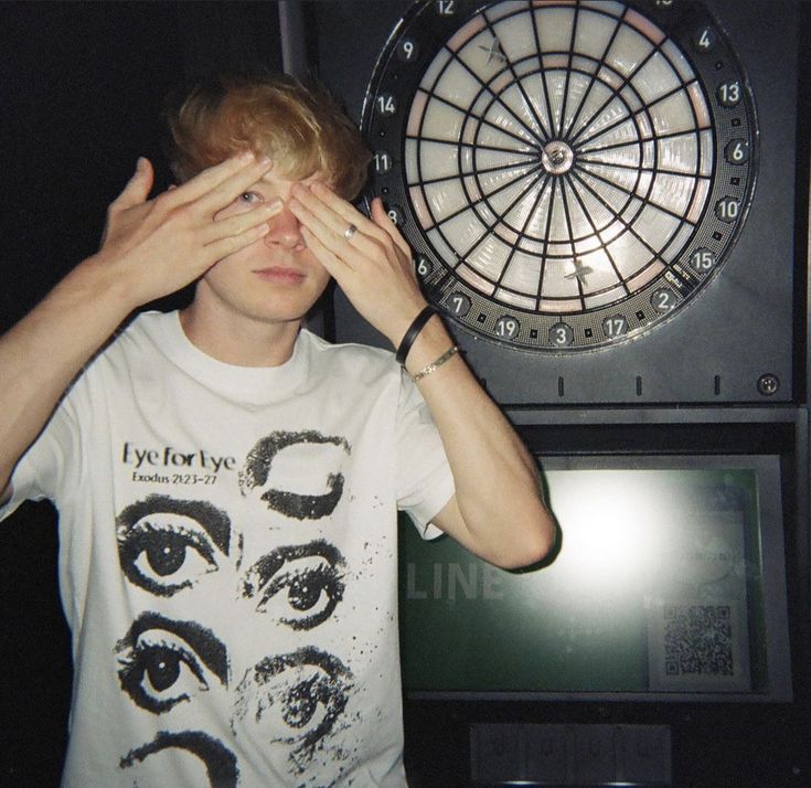 a young man holding his hands up to his eyes in front of a dart board