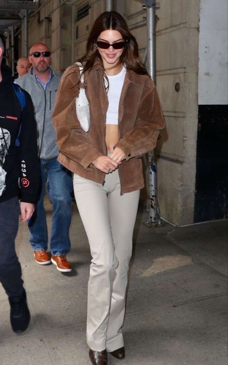 a woman in brown jacket and tan pants walking on sidewalk next to man wearing sunglasses