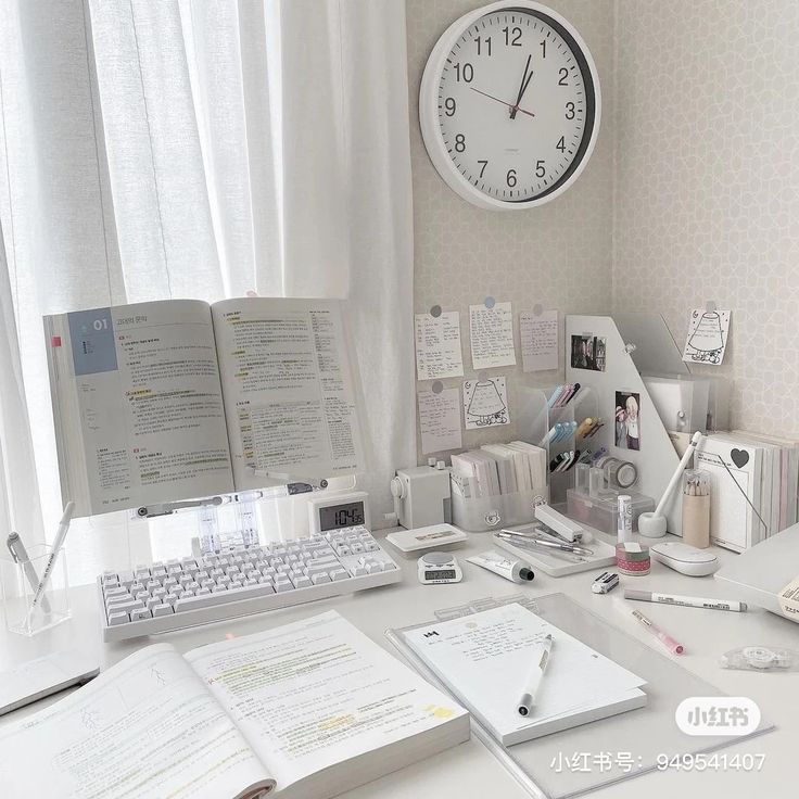 a white desk topped with lots of papers and a computer monitor next to a clock