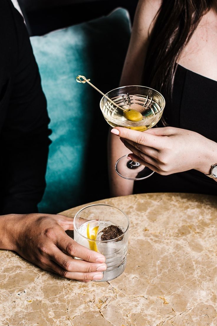 a person holding a drink in their hand at a table with other people sitting around