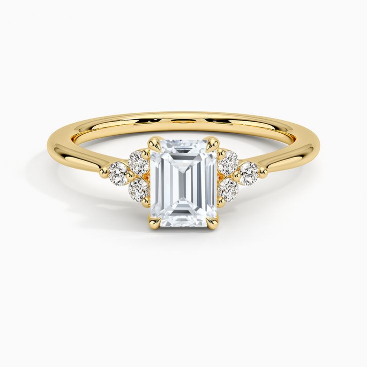 Emerald Cut Melody Diamond Engagement Ring - 18K Yellow Gold. This chic ring features a dazzling cluster of three diamonds framing each side of the center gem. The gently tapering band and open gallery creates a light and lustrous look (1/10 total carat weight). 14k Gold Cluster Diamond Ring With Prong Setting, Yellow Gold Cluster Ring With Cubic Zirconia, Timeless Diamond Emerald Ring For Promise, Timeless Diamond Emerald Promise Ring, Timeless Emerald Ring As Promise Ring, Dazzling Moissanite Cluster Ring With Emerald Cut, 14k Gold Cluster Diamond Promise Ring, Dazzling Emerald Cut Moissanite Cluster Ring, Gold Emerald Cut Cluster Ring With Center Stone