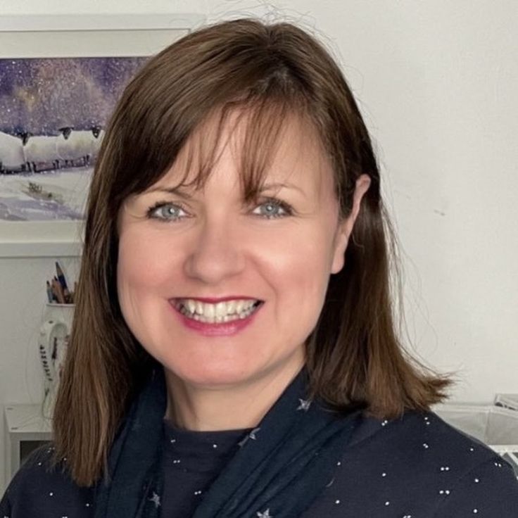 a smiling woman wearing a scarf in front of a wall with pictures on the walls