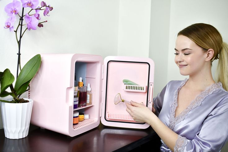 a woman is looking at the contents of a pink mini refrigerator that she's holding