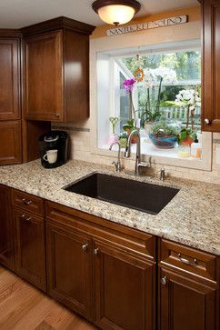 a kitchen with wooden cabinets and granite counter tops in front of a window that has flowers on it