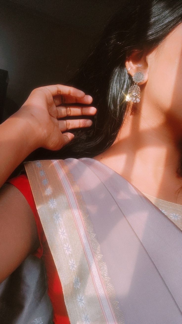 a woman with long black hair wearing a white and gold saree, holding her hand up to her ear