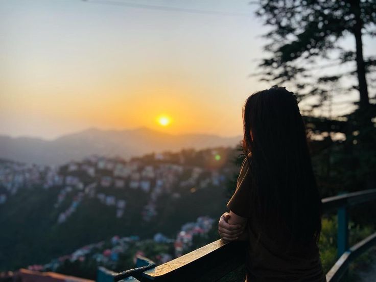 a woman standing on top of a hill looking at the sunset