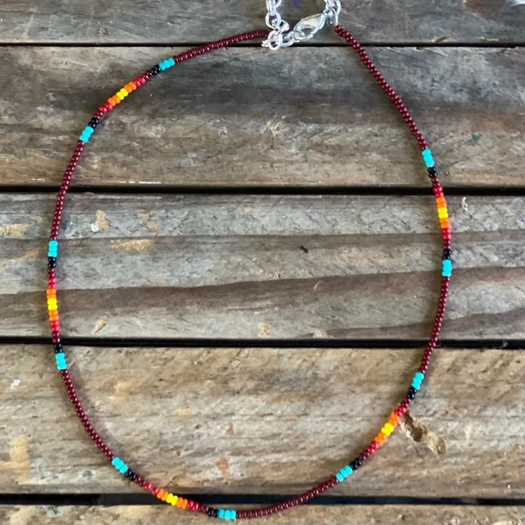 a colorful beaded necklace is sitting on a wooden surface with a silver chain around it