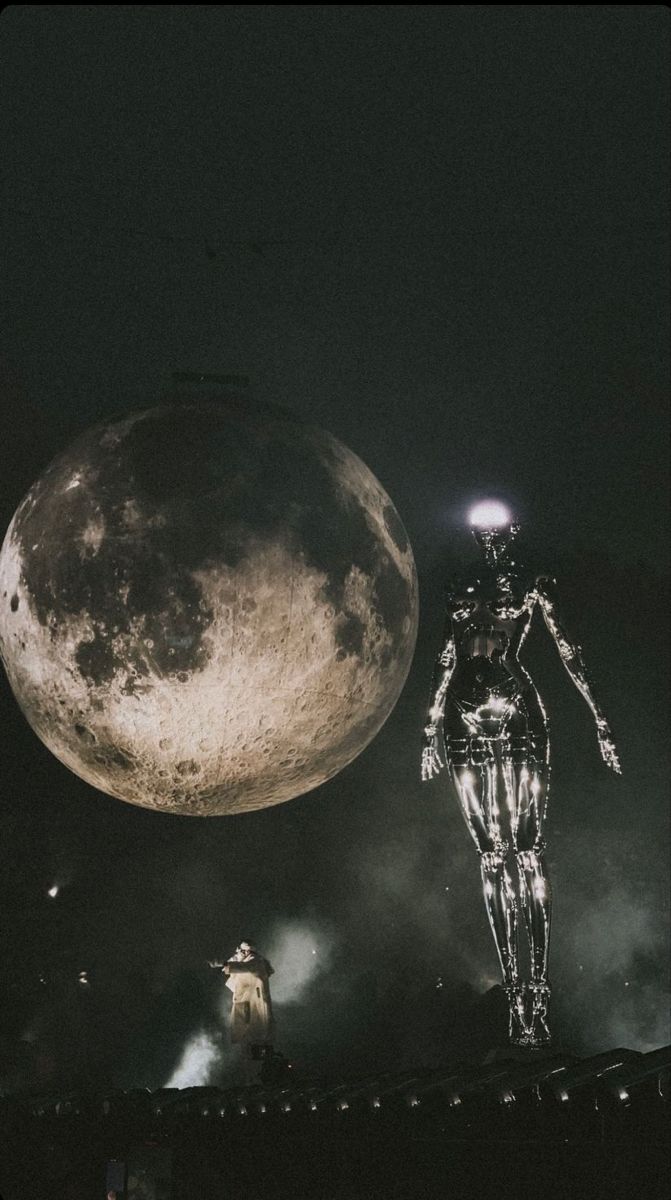 a man standing on top of a stage next to a giant moon in the sky