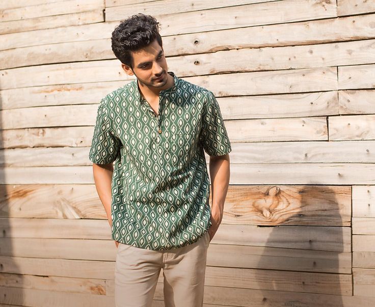 a man standing in front of a wooden wall wearing a green shirt and khaki pants