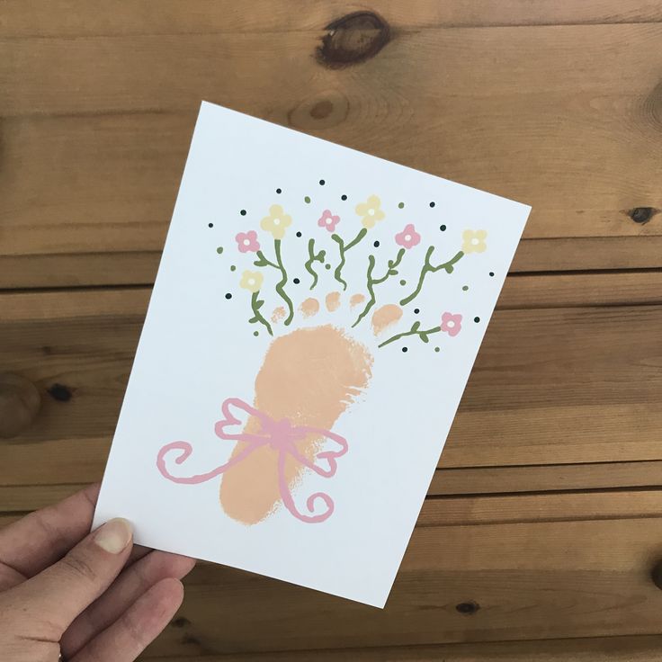 a hand holding up a card with an image of a baby's foot and flowers on it