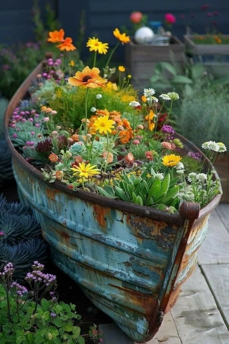 a boat filled with lots of flowers sitting on top of a wooden floor next to plants