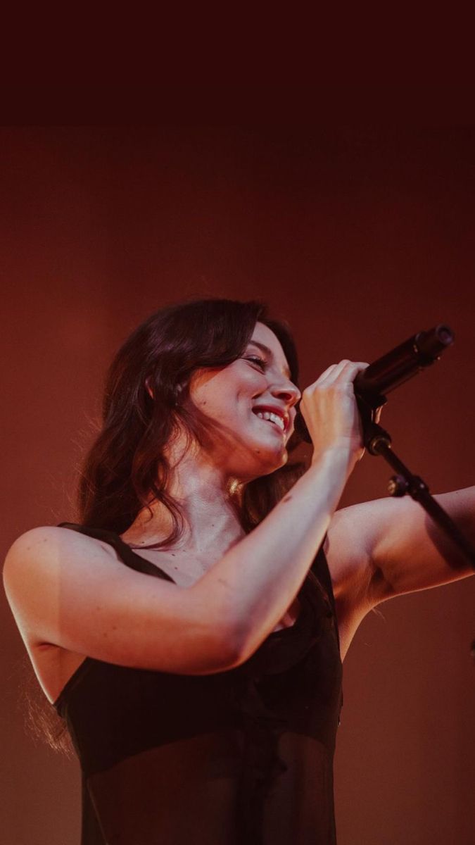 a woman singing into a microphone while holding her arm out to the side with both hands