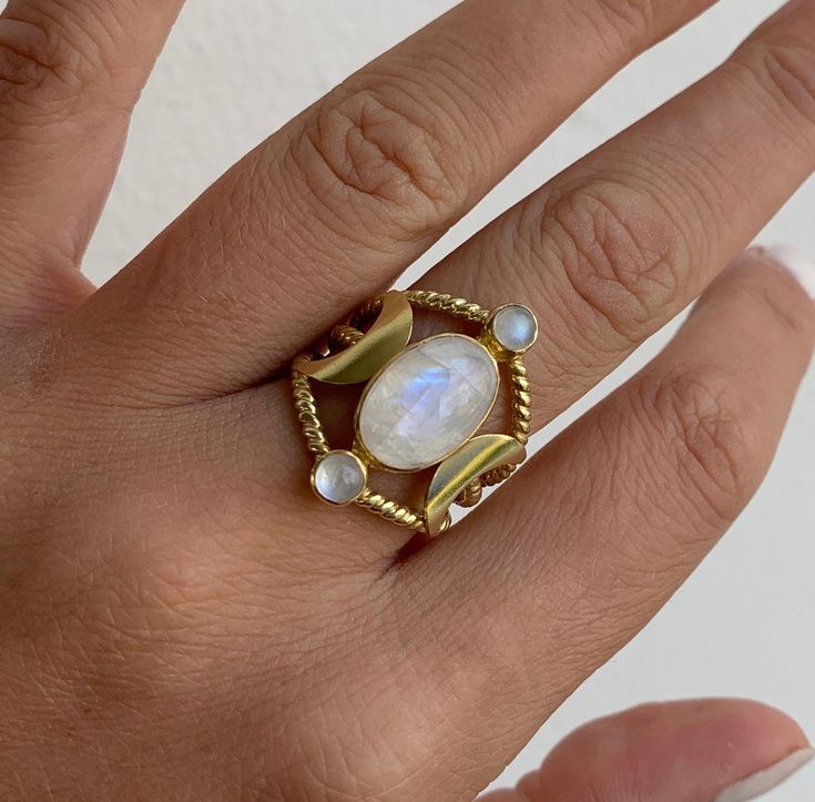 Raina 14K Gold Plated Sterling Silver Rainbow Moonstone Ring One of our forever favourite. This dreamy rings captures the triple goddess symbol as well three beautiful rainbow moonstones. Feminine energy oozes out of this stunning triple banded ring. Our jewels are here to make you feel empowered and radiant. * Deliciously feminine * Triple Goddess Symbol * High quality 2 micron 14K gold plating to premium jewellery standards * High quality Sterling Silver Base * Ethically sourced Rainbow Moonst Celestial Style Moonstone Promise Ring, Ethereal Gold Rings With Gemstones, Ethereal Oval Moonstone Jewelry, Celestial Multi-stone Moonstone Ring, Unique Yellow Gold Moonstone Ring, Celestial Multi-stone Oval Moonstone Ring, Celestial Multi-stone Moonstone Oval Ring, Gold Multi-stone Moonstone Jewelry, Heirloom Style Moonstone Gemstone Ring