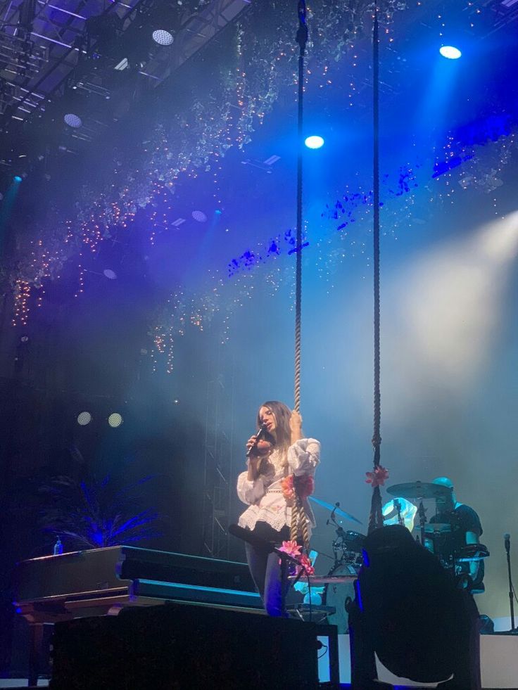 a woman is sitting on a swing in the middle of a stage with blue lights