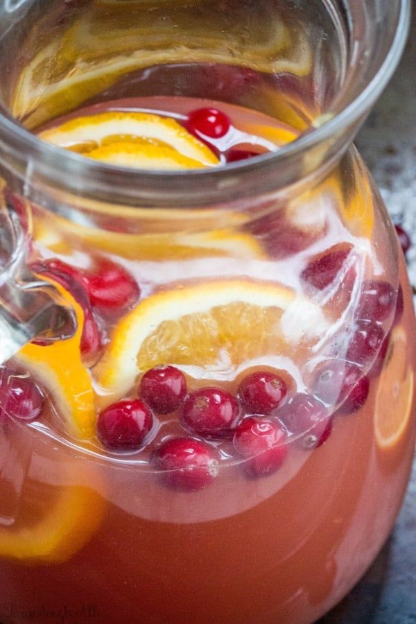 a pitcher filled with liquid sitting on top of a table next to orange slices and cranberries