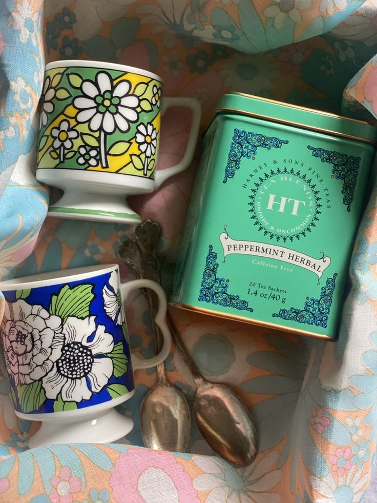 three cups and spoons sitting next to each other on top of a floral blanket