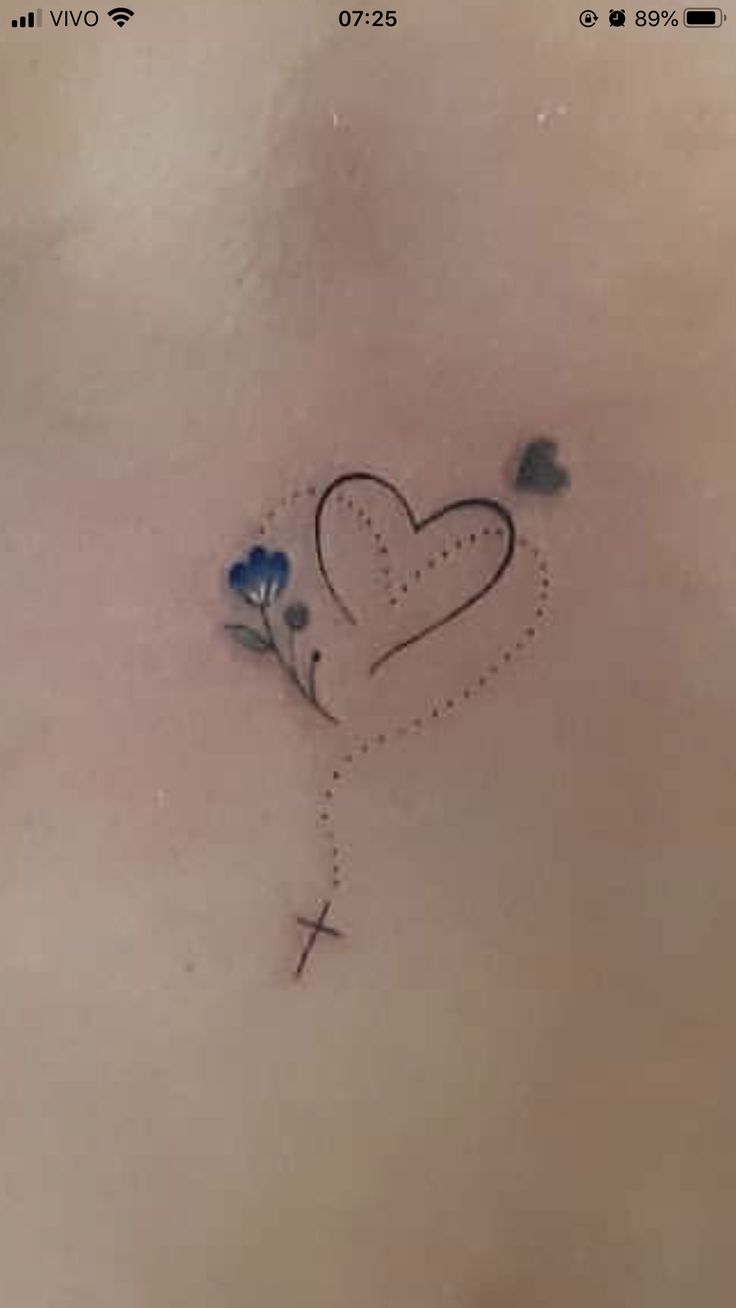 a cross and heart tattoo on the back of a woman's stomach with blue flowers