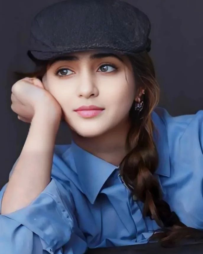 a woman wearing a blue shirt and black hat with her hand on her head, sitting down