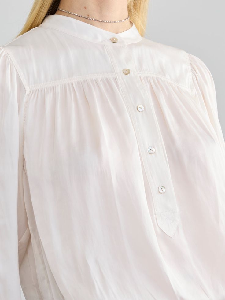 Description:The Roisin blouse is a refined popover top crafted from our wrinkle-resistant Japanese satin. It features full-length, voluminous sleeves, finished with matching natural shell buttons at the cuffs. The front and back yoke has subtle gathering, adding graceful movement and comfort. This blouse looks polished whether worn loose or tucked into pants. Tuck into the Pleated Pull-on Pants for a flowy chic presentation. Size Fit:Model (5’9”) wears a size small Length: 25 1/4"Chest: 20"Sleev Classic Blouse With Balloon Sleeves And Button Cuffs, Bishop Sleeve Tops For Work With Buttons, Elegant Tops With Covered Buttons For Daywear, Classic Formal Tops With Gathered Sleeves, Feminine Tops With Smocked Bishop Sleeves, Cream Blouson Sleeves Top For Daywear, Balloon Sleeve Tops With Button Cuffs For Daywear, Daywear Blouse With Pleated Balloon Sleeves, Chic Tops With Bishop Sleeves And Buttons