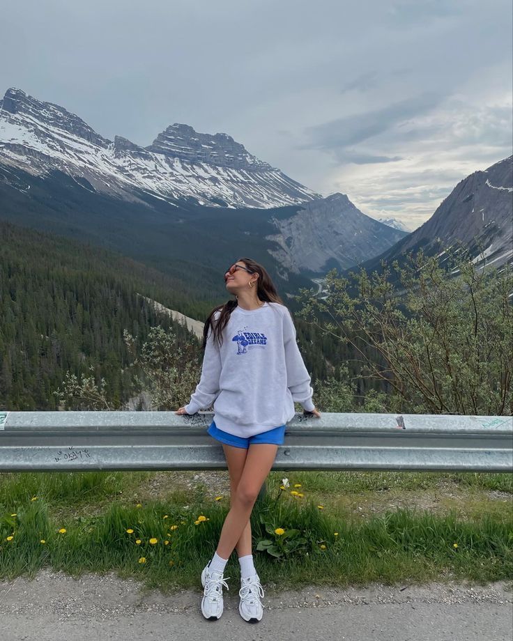 a woman is sitting on a bench looking up at the mountains and snow capped peaks