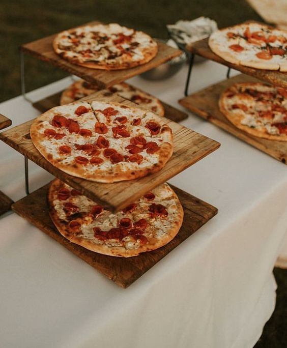 four pizzas on wooden trays sitting on top of a white tablecloth covered table