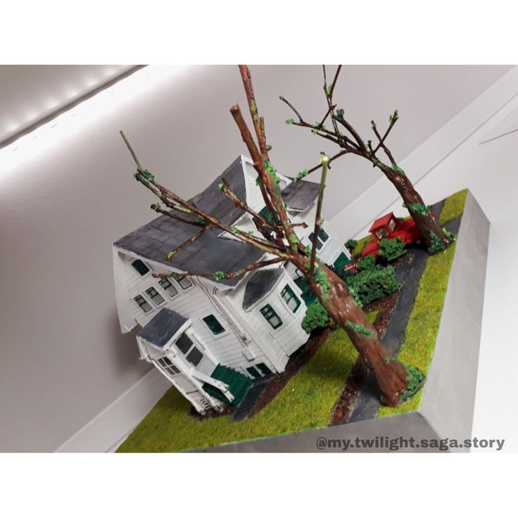 a fake tree is placed in front of a model house on the floor next to a wall