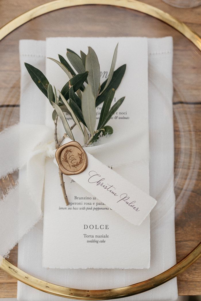 an elegant place setting with white napkins and greenery