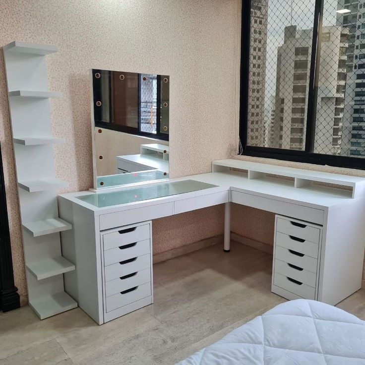 a white desk with drawers and a mirror in a room next to a window that has cityscape on the wall