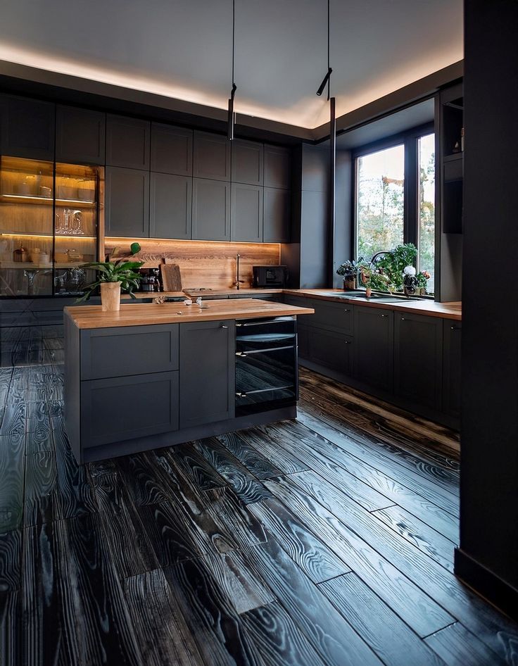 a kitchen with wood flooring and black cabinetry is lit by two pendant lights