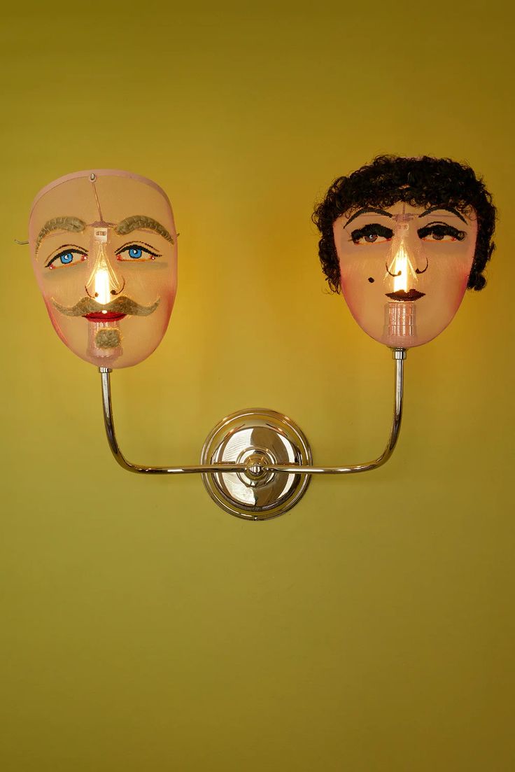 two masks are lit up on the wall, one has a candle in its mouth