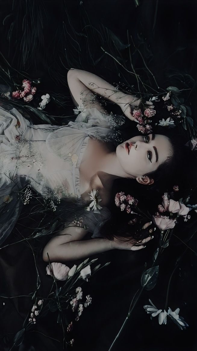 a woman laying on the ground with flowers in her hair and wearing a white dress