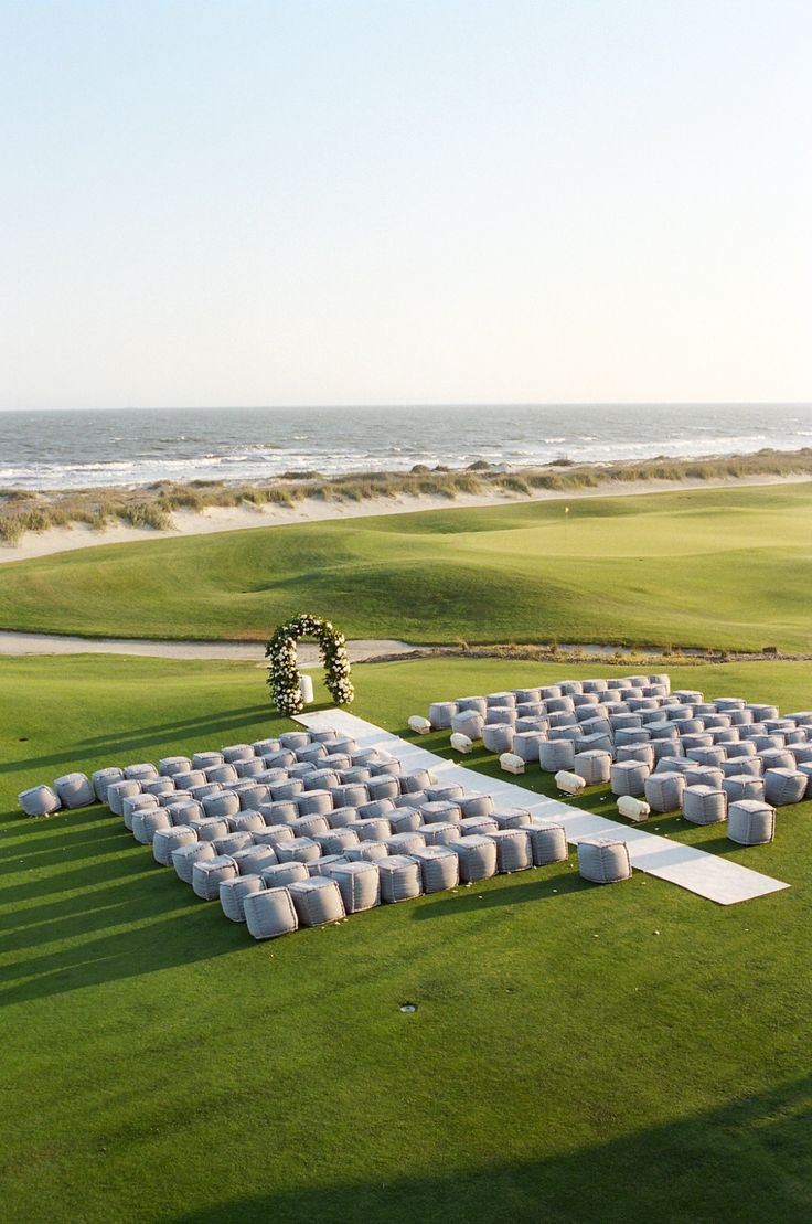 an aerial view of a golf course with rows of white chairs on the grass and ocean in the background